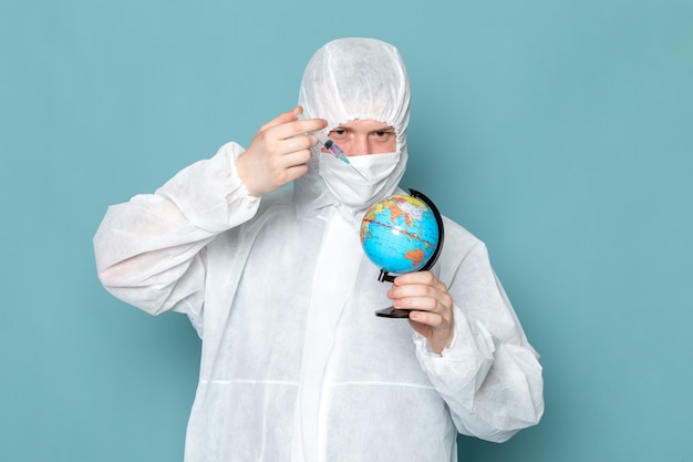 Un hombre joven de vista frontal en traje especial blanco y sosteniendo un pequeño globo en la pared azul traje de hombre peligro color de equipo especial