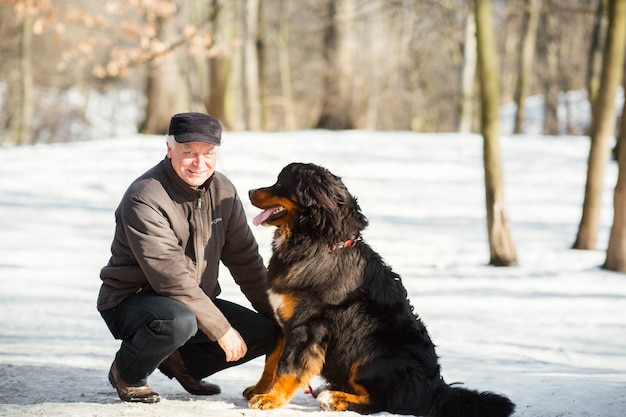 El hombre juega con un divertido perro de montaña de Bernese en la nieve en el parque