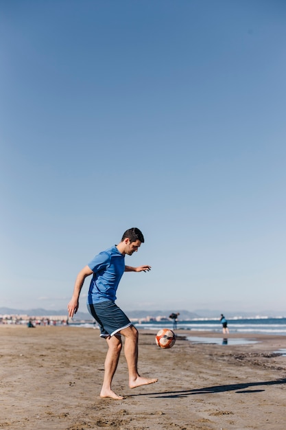 Hombre jugando al fútbol en la playa
