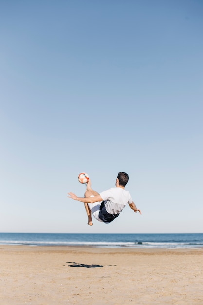 Hombre jugando al fútbol en la playa