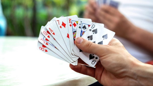 Un hombre jugando a las cartas con otras personas sosteniendo una baraja.