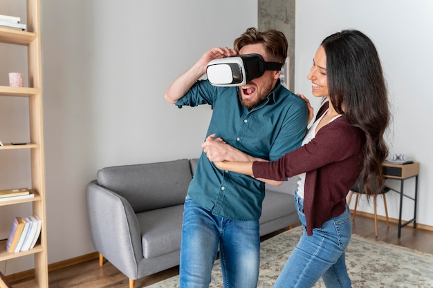 Hombre jugando con casco de realidad virtual en casa junto a la mujer