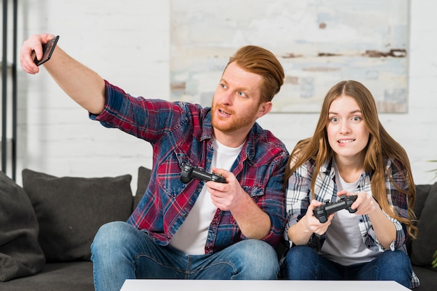 Hombre jugando videojuegos con su novia tomando selfie en smartphone