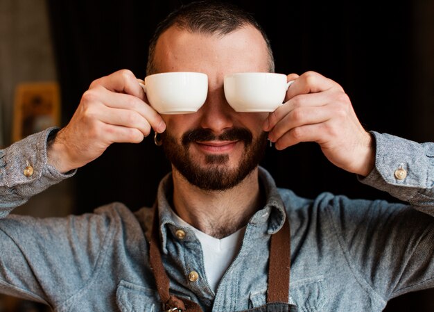 Hombre juguetón posando con tazas de café