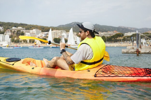 Hombre en kayak con gorra y chaqueta de seguridad amarilla
