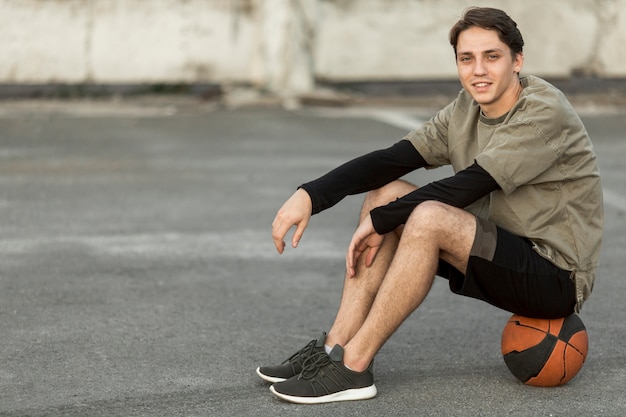 Foto gratuita hombre de lado sentado en una pelota de baloncesto