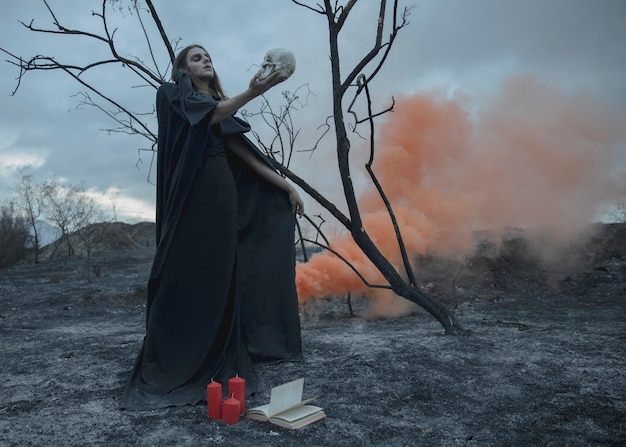 Foto gratuita hombre de lado sosteniendo una calavera y con un libro a sus pies