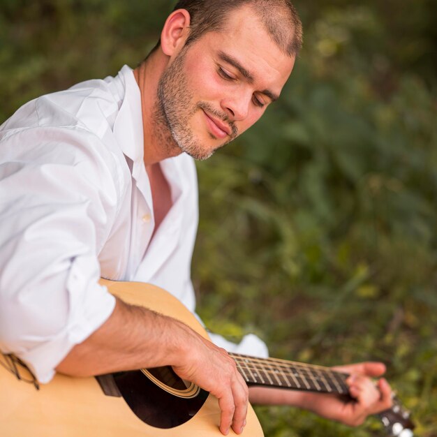 Hombre de lado tocando la guitarra en la naturaleza