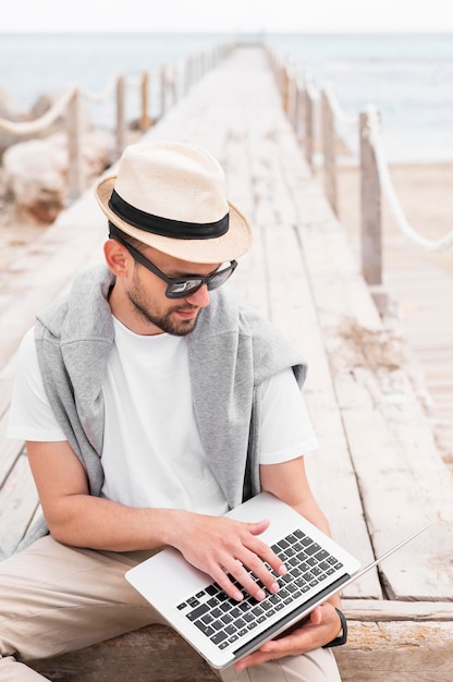 Foto gratuita hombre con laptop en muelle de playa