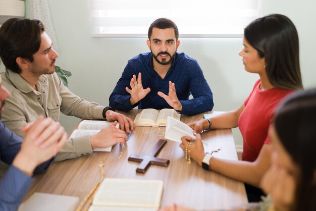 Hombre latino de unos 20 años con mucha fe explicando las sagradas escrituras a hombres y mujeres jóvenes parte de una comunidad religiosa