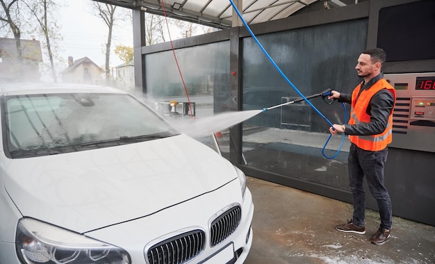 Hombre lavando auto en la estación de lavado de autos con chaleco naranja