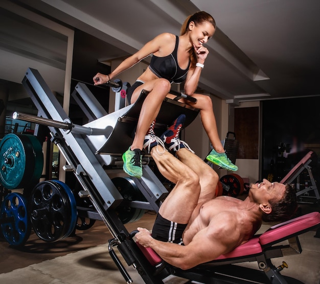 Hombre levantador de pesas haciendo prensas de piernas con su entrenador. La pareja deportiva está haciendo ejercicio en el gimnasio.