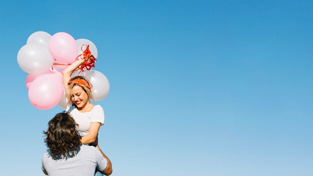Hombre levantando a mujer alegre con globos