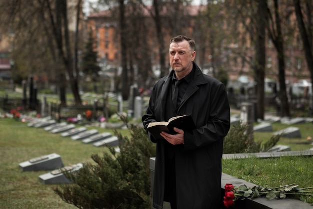 Foto gratuita hombre leyendo de una biblia en una lápida en el cementerio