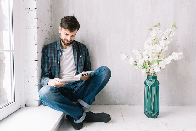 Hombre leyendo libro cerca de la ventana