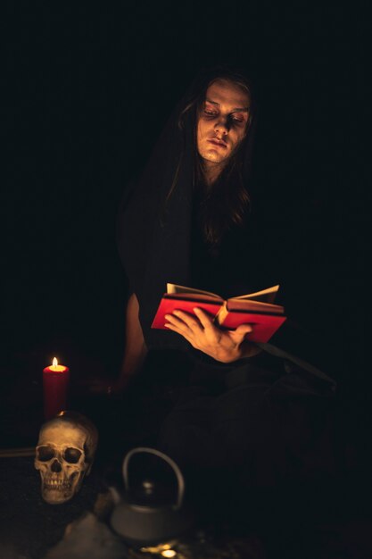 Hombre leyendo un libro de hechizos rojos en la oscuridad