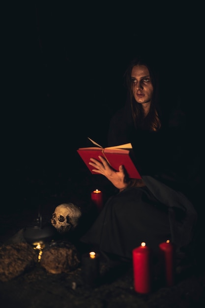 Hombre leyendo un libro de hechizos rojos en la oscuridad