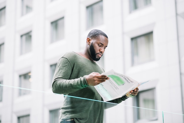 Foto gratuita hombre leyendo periódico cerca de la valla de vidrio