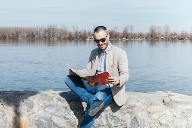 Foto gratuita hombre leyendo revista cerca del agua