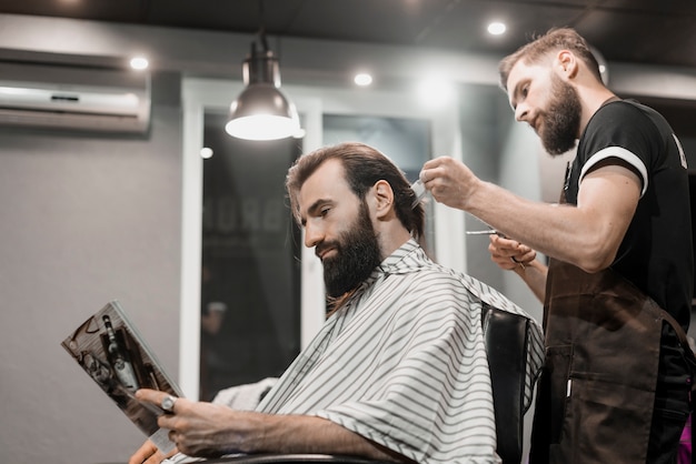 Hombre leyendo revistas mientras corta el pelo en peluquería