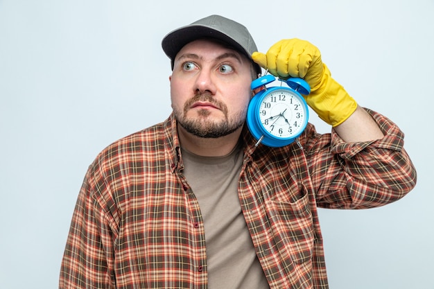 Foto gratuita hombre limpiador ansioso con guantes de goma sosteniendo el despertador y mirando al lado