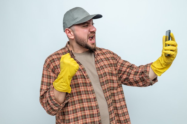 Foto gratuita hombre limpiador eslavo emocionado con guantes de goma manteniendo el puño y mirando el teléfono