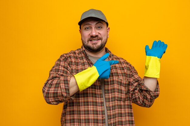 Hombre limpiador eslavo sonriente con guantes de goma apuntando a su mano vacía