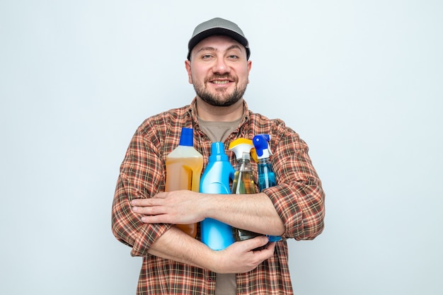 Hombre limpiador eslavo sonriente sosteniendo líquidos y aerosoles de limpieza
