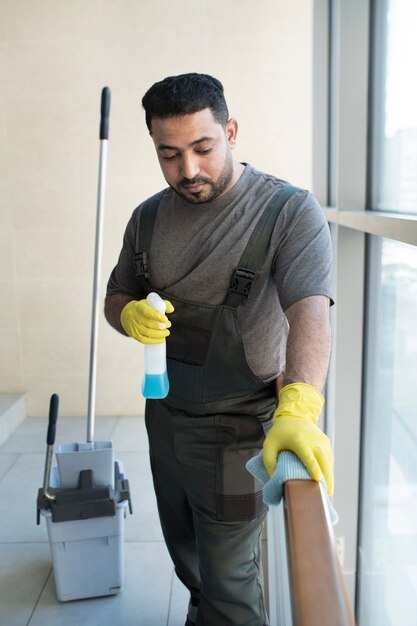 Hombre limpiando barandilla con paño plano medio