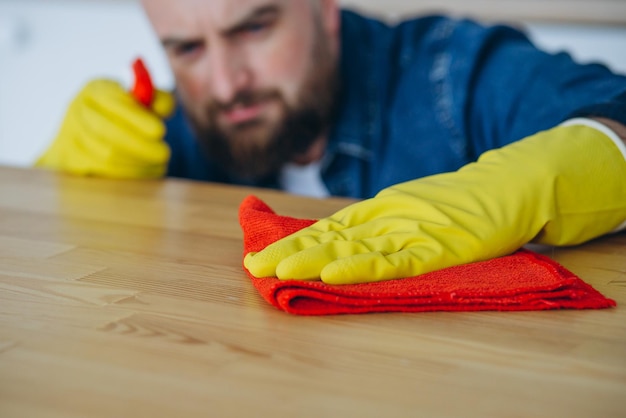 Hombre limpiando en casa usando guantes de goma y usando spray