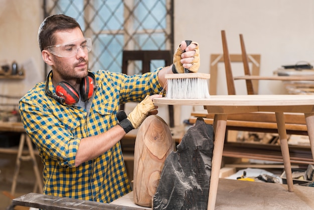 Hombre limpiando madera con cepillo de polvo en tablón de madera en el taller