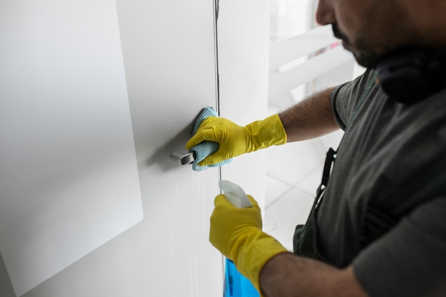 Hombre limpiando el pomo de la puerta con producto