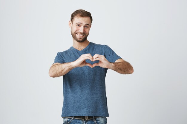 Hombre lindo romántico sonriendo, mostrar signo de corazón