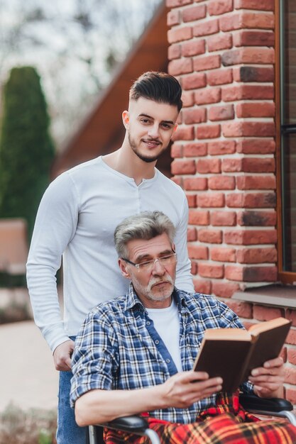 Un hombre lleva a su padre cerca de un hogar de ancianos, se divierten y se ríen mientras leen un libro.