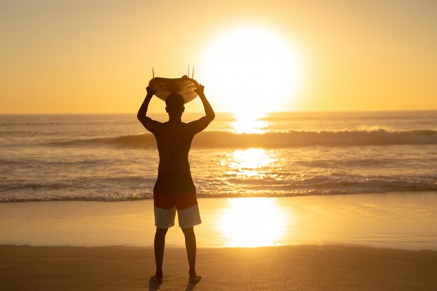 Hombre llevando tabla de surf sobre su cabeza en la playa
