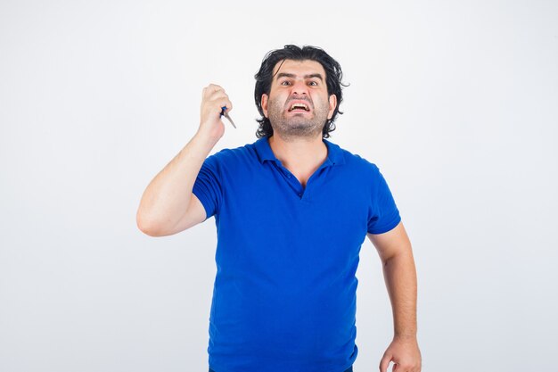 Hombre maduro, amenazando con tijeras en camiseta azul y mirando agresivo, vista frontal.