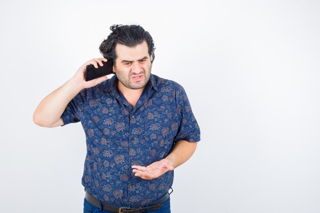 Hombre maduro en camisa hablando por teléfono móvil y mirando enojado, vista frontal.