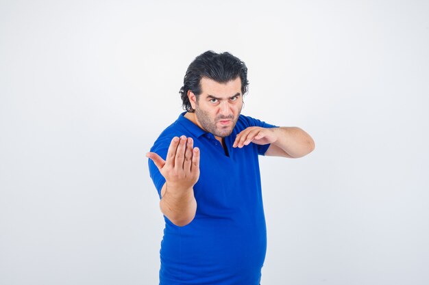 Hombre maduro en camiseta azul, jeans de pie en pose de lucha y mirando enfocado, vista frontal.