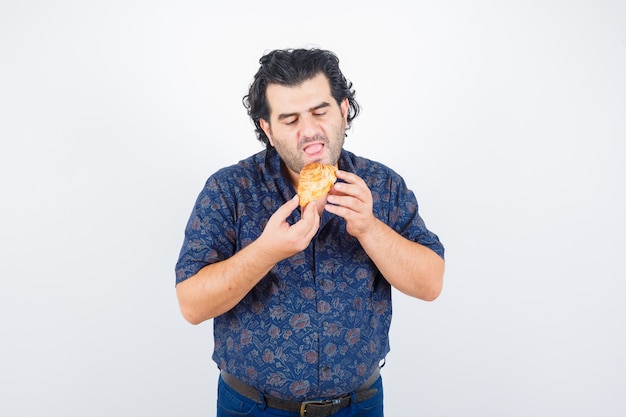 Foto gratuita hombre maduro comiendo productos de pastelería en camisa y mirando hambriento, vista frontal.