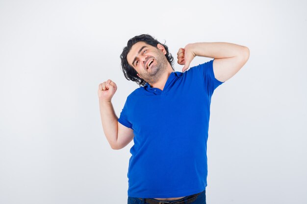 Hombre maduro estirando la parte superior del cuerpo en camiseta azul y mirando relajado, vista frontal.