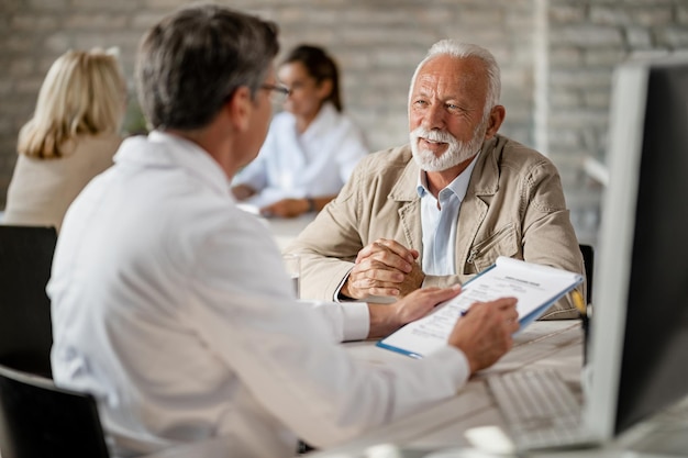 Hombre maduro feliz que tiene consultas con un médico sobre la póliza de seguro de salud durante una reunión en la clínica