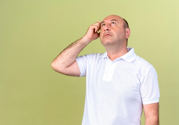 Hombre maduro, mirando hacia arriba pensando en rascarse la cabeza aislado sobre fondo verde oliva
