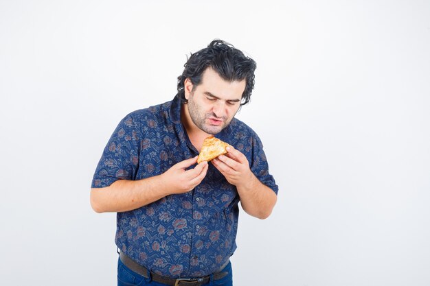 Hombre maduro mirando producto de pastelería en camisa y mirando hambriento. vista frontal.
