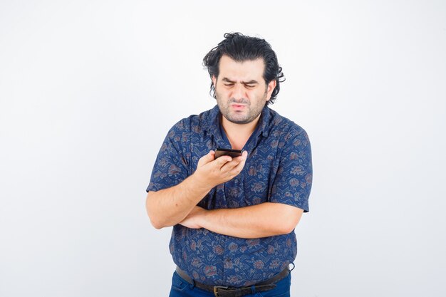 Hombre maduro mirando el teléfono móvil en camisa y mirando pensativo. vista frontal.