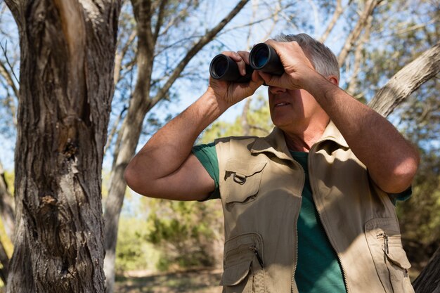 Hombre maduro mirando a través de binoculares en el bosque