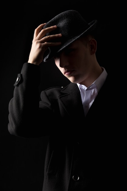 Hombre mafioso guapo tocar el sombrero en la oscuridad