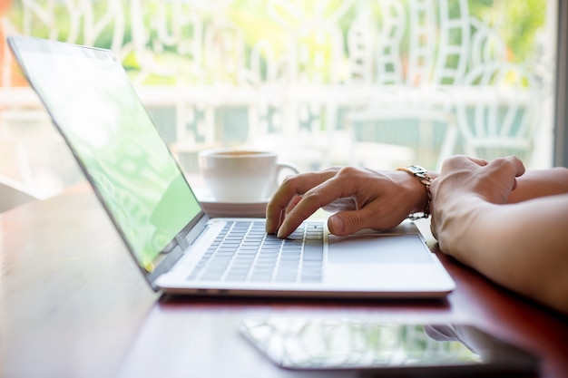 Hombre mano escribiendo en la computadora portátil en la cafetería