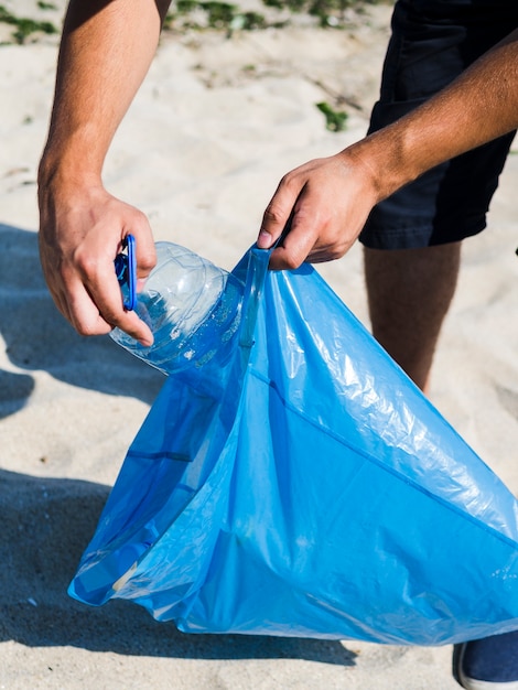 Foto gratuita hombre mano poniendo una botella de plástico transparente en una bolsa de basura azul