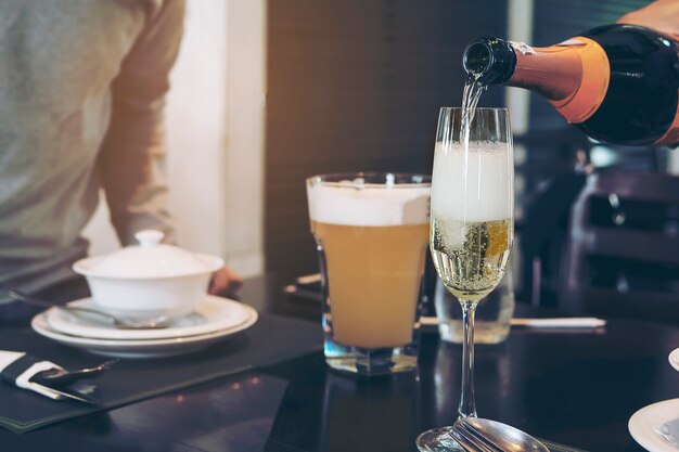 hombre mano vertiendo champán en vaso listo para beber sobre borrosa mesa en restaurante