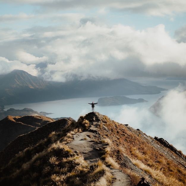 Hombre con las manos abiertas de pie en la cima de una montaña disfrutando de la increíble vista de un lago